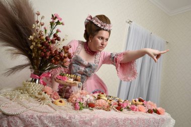 Zengin pembe bir elbise giyen sevimli bir kadın modelin portresi. Tarihi bir Fransız barok asilzadesinin kostümü. Pastalarla, çiçeklerle ve mücevherlerle ziyafet çekiyorlar.