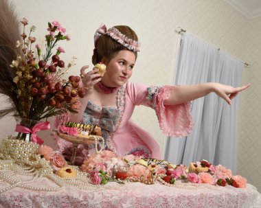 Zengin pembe bir elbise giyen sevimli bir kadın modelin portresi. Tarihi bir Fransız barok asilzadesinin kostümü. Pastalarla, çiçeklerle ve mücevherlerle ziyafet çekiyorlar.