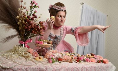 Zengin pembe bir elbise giyen sevimli bir kadın modelin portresi. Tarihi bir Fransız barok asilzadesinin kostümü. Pastalarla, çiçeklerle ve mücevherlerle ziyafet çekiyorlar.