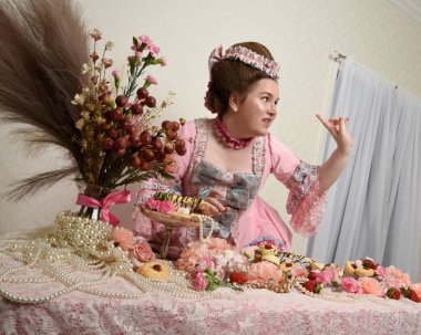 Zengin pembe bir elbise giyen sevimli bir kadın modelin portresi. Tarihi bir Fransız barok asilzadesinin kostümü. Pastalarla, çiçeklerle ve mücevherlerle ziyafet çekiyorlar.