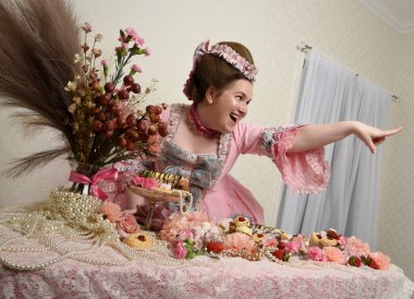 Zengin pembe bir elbise giyen sevimli bir kadın modelin portresi. Tarihi bir Fransız barok asilzadesinin kostümü. Pastalarla, çiçeklerle ve mücevherlerle ziyafet çekiyorlar.