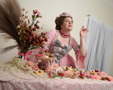 Zengin pembe bir elbise giyen sevimli bir kadın modelin portresi. Tarihi bir Fransız barok asilzadesinin kostümü. Pastalarla, çiçeklerle ve mücevherlerle ziyafet çekiyorlar.