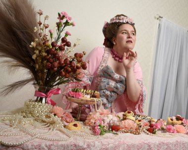 Zengin pembe bir elbise giyen sevimli bir kadın modelin portresi. Tarihi bir Fransız barok asilzadesinin kostümü. Pastalarla, çiçeklerle ve mücevherlerle ziyafet çekiyorlar.