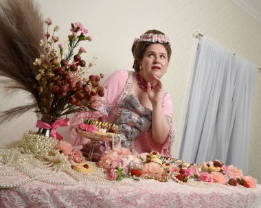 Zengin pembe bir elbise giyen sevimli bir kadın modelin portresi. Tarihi bir Fransız barok asilzadesinin kostümü. Pastalarla, çiçeklerle ve mücevherlerle ziyafet çekiyorlar.