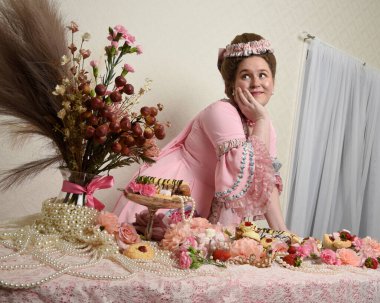 Zengin pembe bir elbise giyen sevimli bir kadın modelin portresi. Tarihi bir Fransız barok asilzadesinin kostümü. Pastalarla, çiçeklerle ve mücevherlerle ziyafet çekiyorlar.