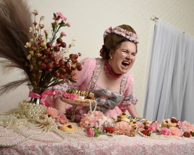 Zengin pembe bir elbise giyen sevimli bir kadın modelin portresi. Tarihi bir Fransız barok asilzadesinin kostümü. Pastalarla, çiçeklerle ve mücevherlerle ziyafet çekiyorlar.