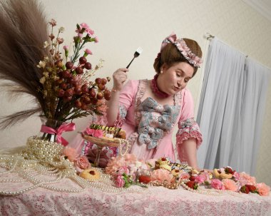 Zengin pembe bir elbise giyen sevimli bir kadın modelin portresi. Tarihi bir Fransız barok asilzadesinin kostümü. Pastalarla, çiçeklerle ve mücevherlerle ziyafet çekiyorlar.