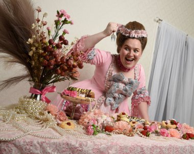 Zengin pembe bir elbise giyen sevimli bir kadın modelin portresi. Tarihi bir Fransız barok asilzadesinin kostümü. Pastalarla, çiçeklerle ve mücevherlerle ziyafet çekiyorlar.