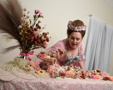 Zengin pembe bir elbise giyen sevimli bir kadın modelin portresi. Tarihi bir Fransız barok asilzadesinin kostümü. Pastalarla, çiçeklerle ve mücevherlerle ziyafet çekiyorlar.