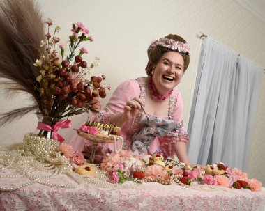 Zengin pembe bir elbise giyen sevimli bir kadın modelin portresi. Tarihi bir Fransız barok asilzadesinin kostümü. Pastalarla, çiçeklerle ve mücevherlerle ziyafet çekiyorlar.