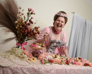 Zengin pembe bir elbise giyen sevimli bir kadın modelin portresi. Tarihi bir Fransız barok asilzadesinin kostümü. Pastalarla, çiçeklerle ve mücevherlerle ziyafet çekiyorlar.