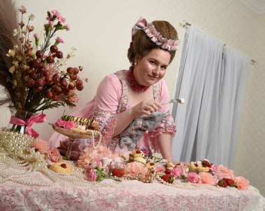 Zengin pembe bir elbise giyen sevimli bir kadın modelin portresi. Tarihi bir Fransız barok asilzadesinin kostümü. Pastalarla, çiçeklerle ve mücevherlerle ziyafet çekiyorlar.