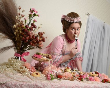 Zengin pembe bir elbise giyen sevimli bir kadın modelin portresi. Tarihi bir Fransız barok asilzadesinin kostümü. Pastalarla, çiçeklerle ve mücevherlerle ziyafet çekiyorlar.