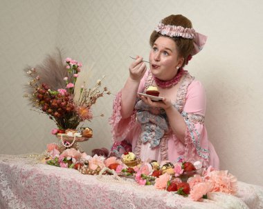 Zengin pembe bir elbise giyen sevimli bir kadın modelin portresi. Tarihi bir Fransız barok asilzadesinin kostümü. Hoşgörülü bir ziyafette tatlı ve zengin yiyeceklerle pasta yemek..