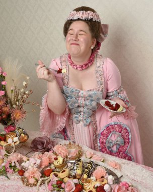 Zengin pembe bir elbise giyen sevimli bir kadın modelin portresi. Tarihi bir Fransız barok asilzadesinin kostümü. Hoşgörülü bir ziyafette tatlı ve zengin yiyeceklerle pasta yemek..