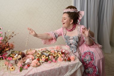 Zengin pembe bir elbise giyen sevimli bir kadın modelin portresi. Tarihi bir Fransız barok asilzadesinin kostümü. Tatlı kekler ve hoşgörülü yemek ziyafetiyle dolu bir masa..