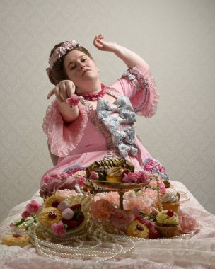 Zengin pembe bir elbise giyen sevimli bir kadın modelin portresi. Tarihi bir Fransız barok asilzadesinin kostümü. Tatlı kekler ve hoşgörülü yemek ziyafetiyle masada oturuyor..