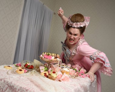 Zengin pembe bir elbise giyen sevimli bir kadın modelin portresi. Tarihi bir Fransız barok asilzadesinin kostümü. Tatlı kekler ve hoşgörülü yemek ziyafetiyle masada oturuyor..