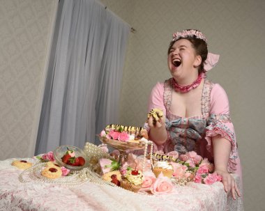 Zengin pembe bir elbise giyen sevimli bir kadın modelin portresi. Tarihi bir Fransız barok asilzadesinin kostümü. Tatlı kekler ve hoşgörülü yemek ziyafetiyle masada oturuyor..