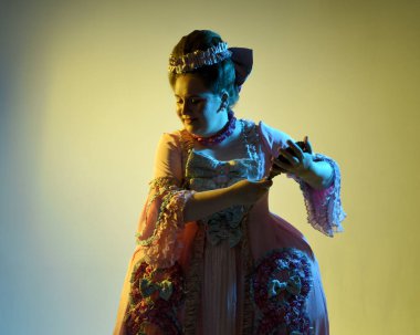  Gösterişli pembe bir elbise giyen kadın modelin sinematik portresi, tarihi bir Fransız barok asaleti kostümü, Marie Antoinette tarzı. Stüdyonun arka planında el aynası var..