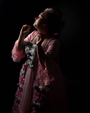 Zengin pembe bir elbise giyen kadın modelin profil portresi, tarihi bir Fransız barok asaleti kostümü, Marie Antoinette tarzı. İzole edilmiş koyu renkli sinematik siluet stüdyo arka planı
