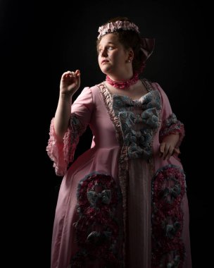 Zengin pembe bir elbise giyen kadın modelin profil portresi, tarihi bir Fransız barok asaleti kostümü, Marie Antoinette tarzı. İzole edilmiş koyu renkli sinematik siluet stüdyo arka planı
