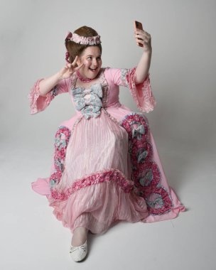 Marie Antoinette tarzı, Fransız barok asilzadelerinin gösterişli pembe elbisesini giyen kadın model. Modern cep telefonu teknolojisiyle tahtta oturmak.