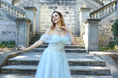 Peri masalı elf prensesi gibi mavi fantezi balo elbisesi giyen güzel bir kadın modelin yakın portresi. Zarif bir poz, romantik bir şatonun merdivenlerinin terasına uzanan hareketli eller..