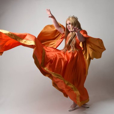 Uzun sarı saçlı, orta çağ fantezi elbisesi giyen, uzun kollu, kraliyet kraliçesinin altın tacını takan uzun boylu bir kadının tam boy portresi. Stüdyo arka planında izole edilmiş, el kol hareketleriyle poz vermek.