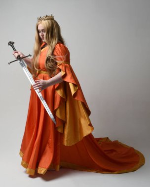 Orta çağ fantezi elbisesi giymiş, büyük boy sarışın kadın portresi, kraliyet kraliçesinin altın tacı. Kılıç tutan poz, izole stüdyo arka planı..