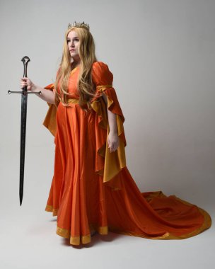 Orta çağ fantezi elbisesi giymiş, büyük boy sarışın kadın portresi, kraliyet kraliçesinin altın tacı. Kılıç tutan poz, izole stüdyo arka planı..