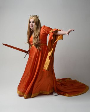 Orta çağ fantezi elbisesi giymiş, büyük boy sarışın kadın portresi, kraliyet kraliçesinin altın tacı. Kılıç tutan poz, izole stüdyo arka planı..