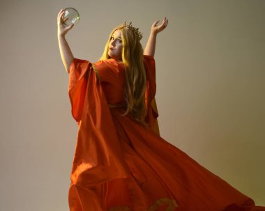 Orta çağ fantezi elbisesi giyen, kraliyet kraliçesinin altın tacını takan iri yarı sarışın bir kadının portresi. Sihirli kristal kahin küresi tutan hareketli eller, izole edilmiş stüdyo arka planı.