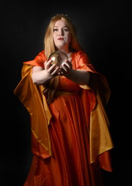 Orta çağ fantezi elbisesi giyen, kraliyet kraliçesi tacını giymiş, iri yarı sarışın bir kadının portresi. Sihirli kristal kahin küresi, izole koyu siyah stüdyo arka planı.