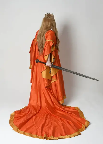 Full length portrait of plus size blonde woman, wearing historical medieval fantasy gown, golden crown  royal queen. Standing pose backview, holding sword weapon, isolated studio background.