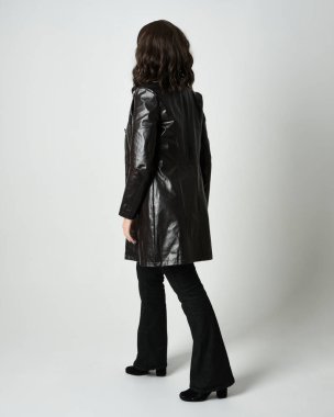 Uzun deri ceket ve siyah çizmeler giyen esmer kadının tam boy portresi. Kameradan uzaklaşıp, geriye dönük poz vermek. Beyaz stüdyo arka planında izole edilmiş siluet..