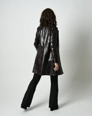 Uzun deri ceket ve siyah çizmeler giyen esmer kadının tam boy portresi. Kameradan uzaklaşıp, geriye dönük poz vermek. Beyaz stüdyo arka planında izole edilmiş siluet..