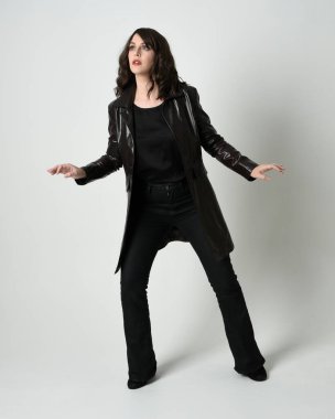 Uzun siyah deri trençkot giyen güzel esmer kadının tam boy portresi, kara film dedektifi. Poz vermek, kameraya doğru yürümek, uzanmak. İzole edilmiş beyaz stüdyo arka planı