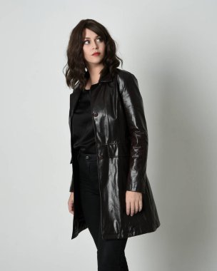 Uzun siyah deri trençkot giyen güzel esmer kadının portresi, kara film dedektifi. Stüdyonun arka planında tek başına poz veriyor.