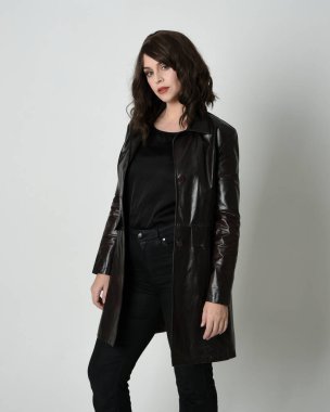 Uzun siyah deri trençkot giyen güzel esmer kadının portresi, kara film dedektifi. Stüdyonun arka planında tek başına poz veriyor.