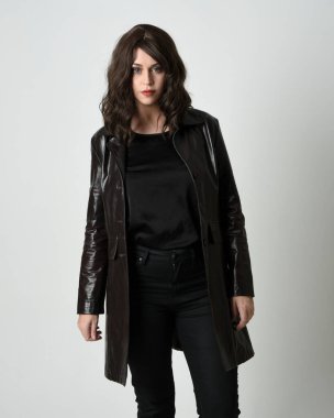 Uzun siyah deri trençkot giyen güzel esmer kadının portresi, kara film dedektifi. Stüdyonun arka planında tek başına poz veriyor.