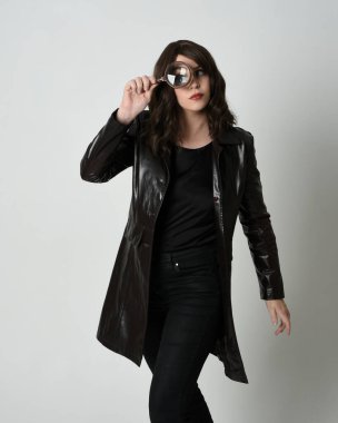 Siyah deri trençkot giyen güzel esmer kadının portresi. Dedektifin büyüteçini tutuyor, kameraya uzanıyor ve bir şey arıyor. İzole stüdyo geçmişi