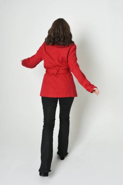 Güzel esmer kadın modelin tam boy portresi, kırmızı trençkot ceketli deri pantolon giyiyor. Arka planda durup kameraya doğru yürüyorsun. Beyaz stüdyo arka planında izole edilmiş siluet.