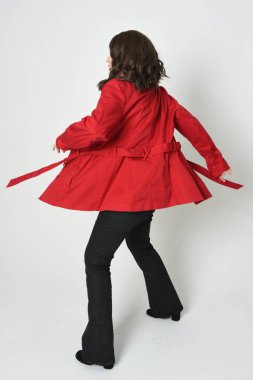 Güzel esmer kadın modelin tam boy portresi, kırmızı trençkot ceketli deri pantolon giyiyor. Arka planda durup kameraya doğru yürüyorsun. Beyaz stüdyo arka planında izole edilmiş siluet.