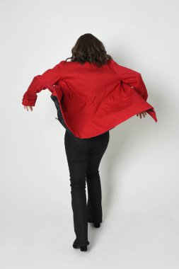 Güzel esmer kadın modelin tam boy portresi, kırmızı trençkot ceketli deri pantolon giyiyor. Arka planda durup kameraya doğru yürüyorsun. Beyaz stüdyo arka planında izole edilmiş siluet.