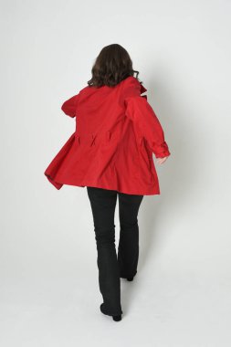 Güzel esmer kadın modelin tam boy portresi, kırmızı trençkot ceketli deri pantolon giyiyor. Arka planda durup kameraya doğru yürüyorsun. Beyaz stüdyo arka planında izole edilmiş siluet.