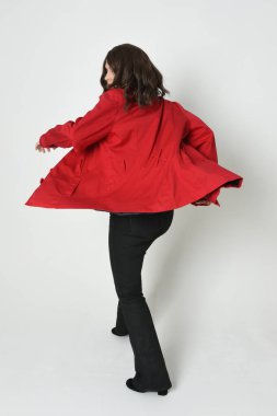 Güzel esmer kadın modelin tam boy portresi, kırmızı trençkot ceketli deri pantolon giyiyor. Arka planda durup kameraya doğru yürüyorsun. Beyaz stüdyo arka planında izole edilmiş siluet.