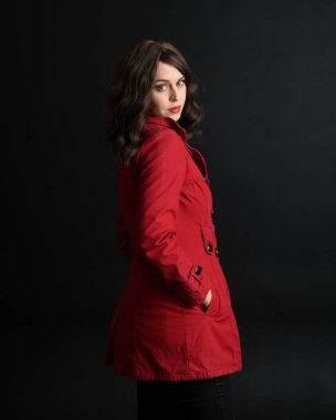 Kırmızı trençkot giyen güzel esmer kadın modelin yakın plan portresi. Karanlık stüdyo arka planında gölgelerle izole edilmiş. arka plan, kameradan uzaklaşıyor.