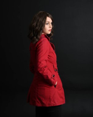 Kırmızı trençkot giyen güzel esmer kadın modelin yakın plan portresi. Karanlık stüdyo arka planında gölgelerle izole edilmiş. arka plan, kameradan uzaklaşıyor.