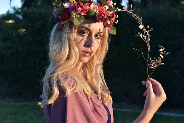 stock image close up portrait of pretty blonde female model wearing a flower crown wreath and purple dress.  green nature  plants and trees in background